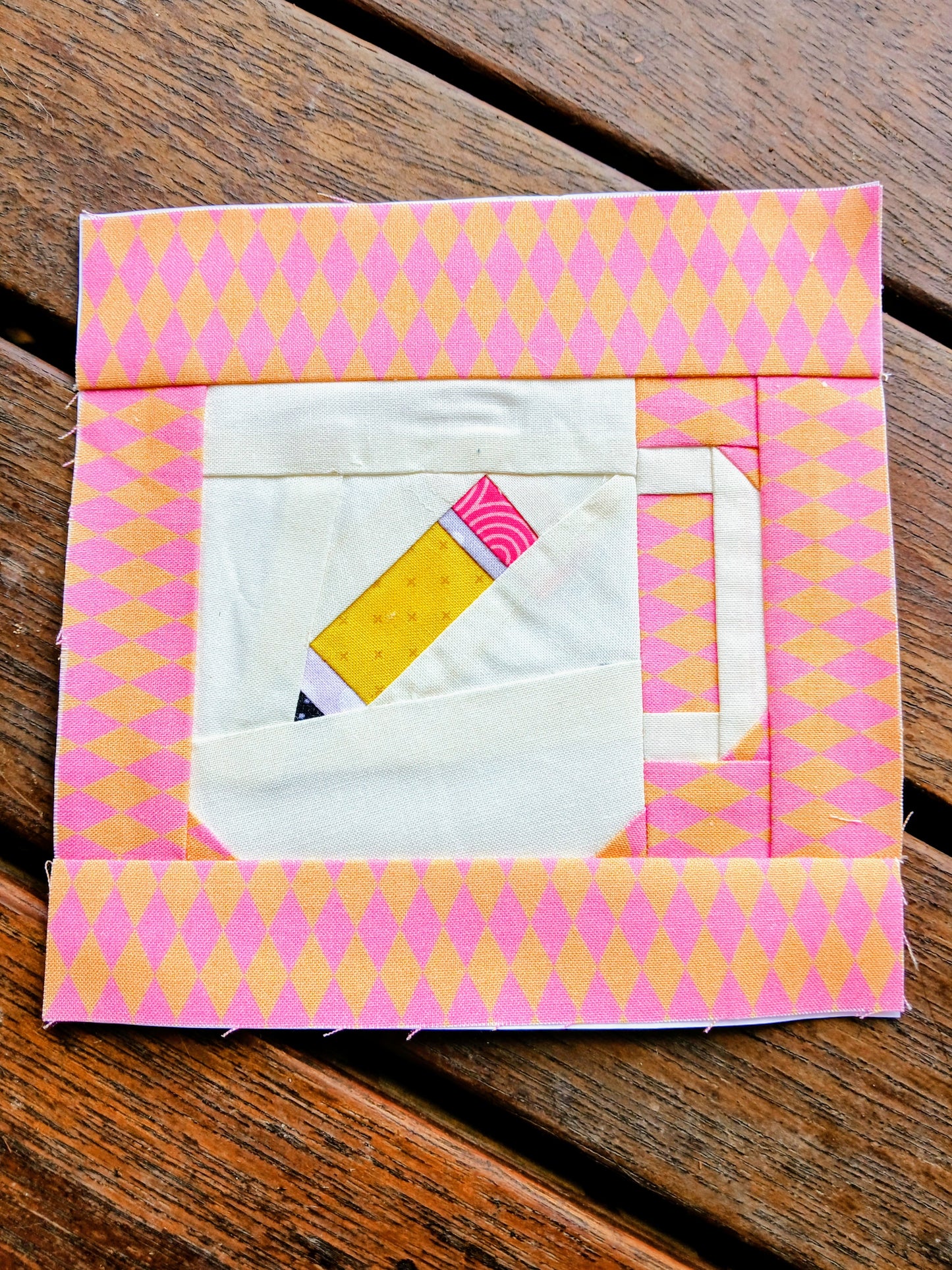 Quilt block with pink and yellow pattern on a wooden surface