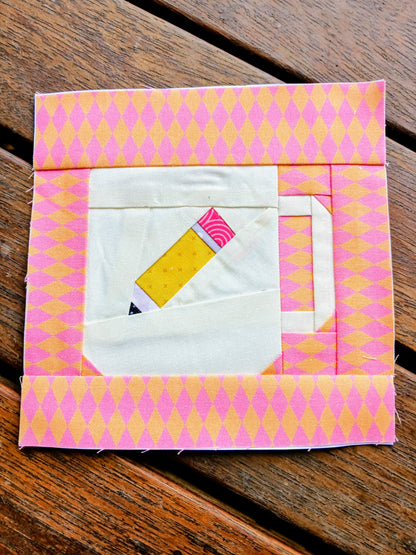 Quilt block with pink and yellow pattern on a wooden surface