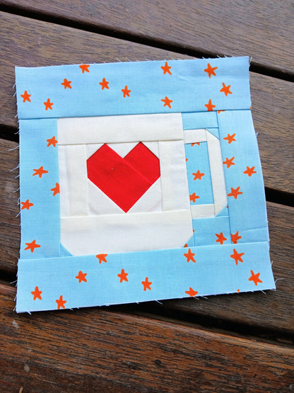 Fabric patch with a red heart and white mug on a blue background with orange stars, placed on a wooden surface.